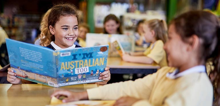 Reading_Hour_primary Little girl smiles as she reads the book I'm Australian Too by Mem Fox.